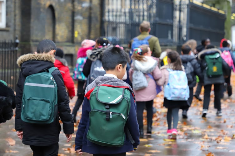 Multi-Cultural Children (asian, Indian, Chinese, Caucasian) primary student or kids and teacher carrying school bag walk in street in rain winter day, with maple leaves on ground. back view