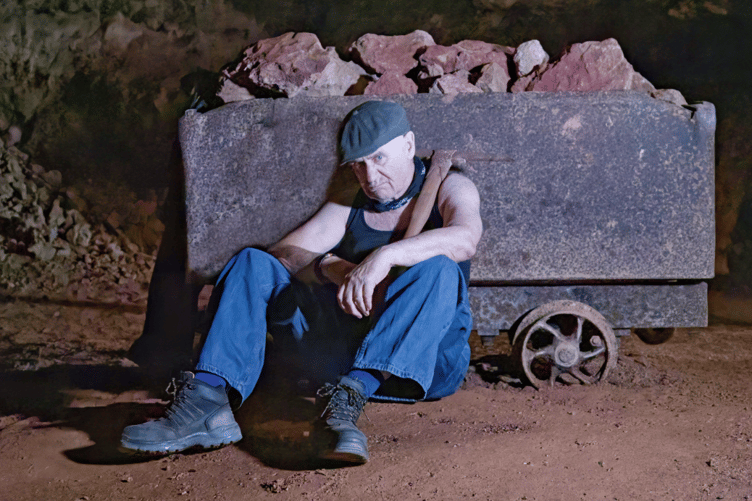 A model portrays a weary miner taking a well-earned rest beside a loaded mine cart during the historical recreation at Clearwell Caves.