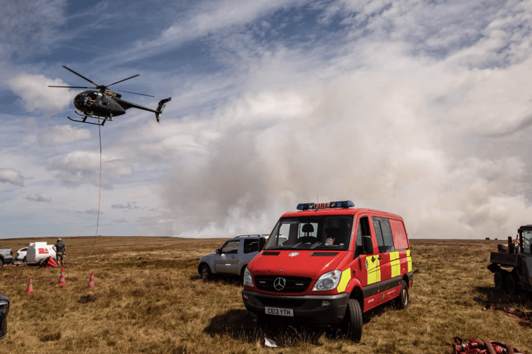 A helicopter joins the firefighting operation as emergency crews tackle a wildfire across open ground in South Wales.